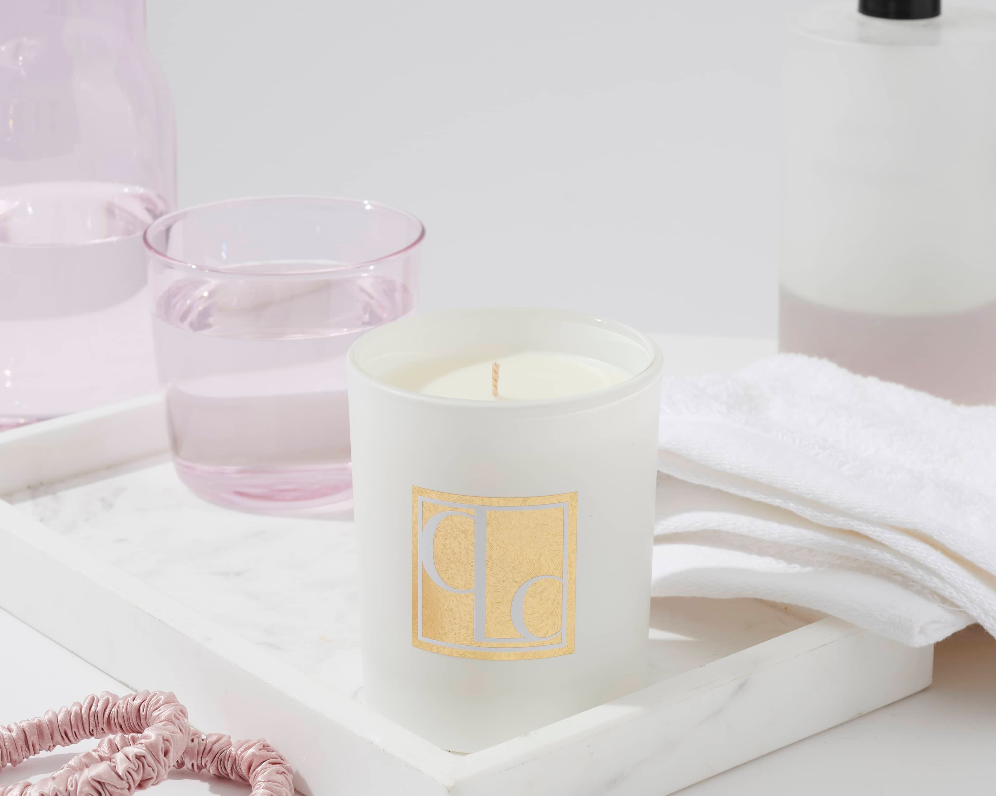 Caitlin Louise Collection Japanese Honeysuckle scented candle on a tray surrounded by light pink scrunchies, hand towel, pink glass filled with water and hand pump - bathroom scene.