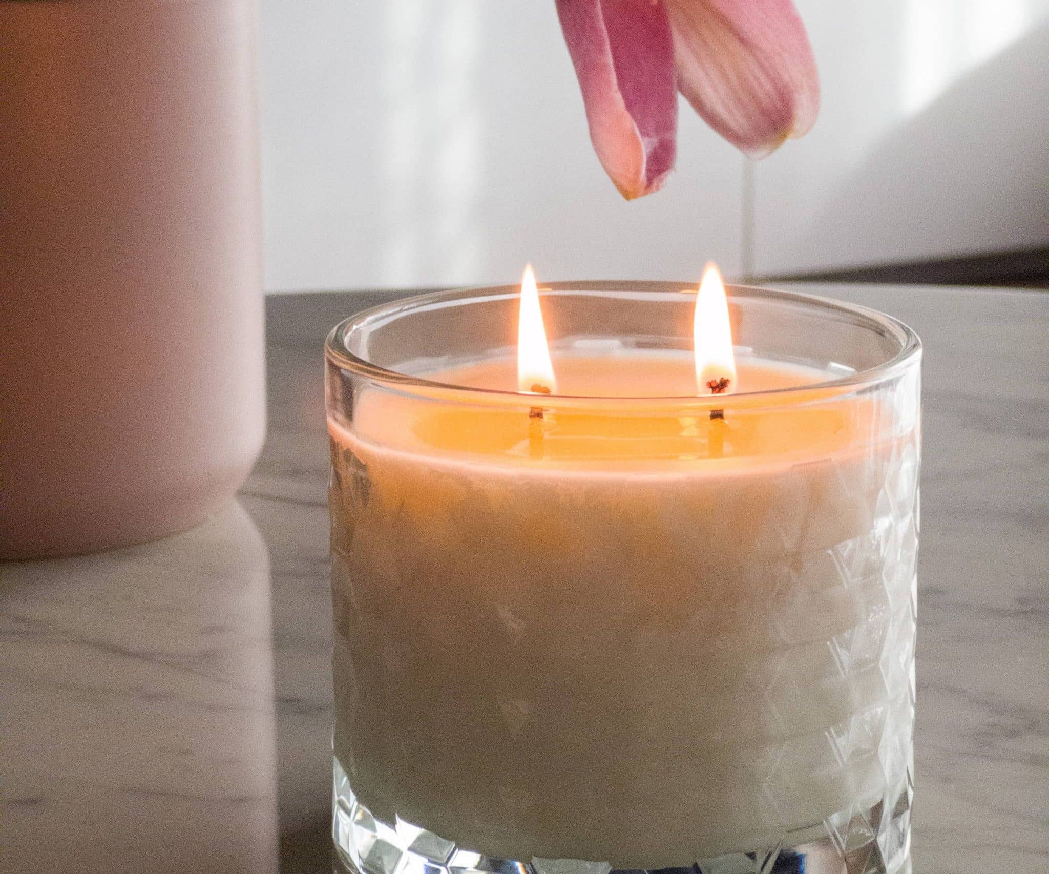 Caitlin Louise Collection limited edition jasmine berry bliss candle - lit flames - sitting on marble coffee table with flowers