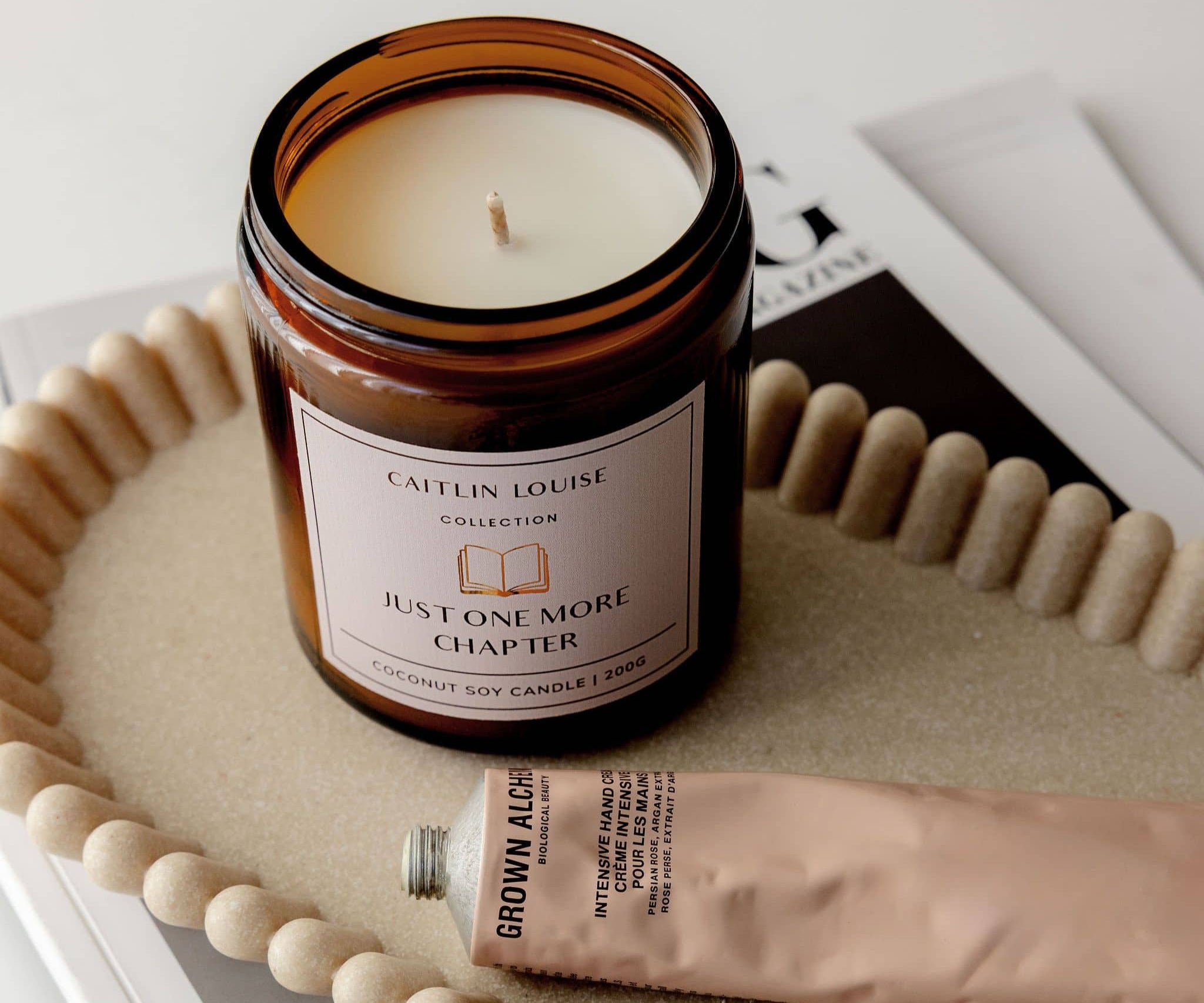 Candle in a glass jar with a label saying "Just One More Chapter" on a textured surface