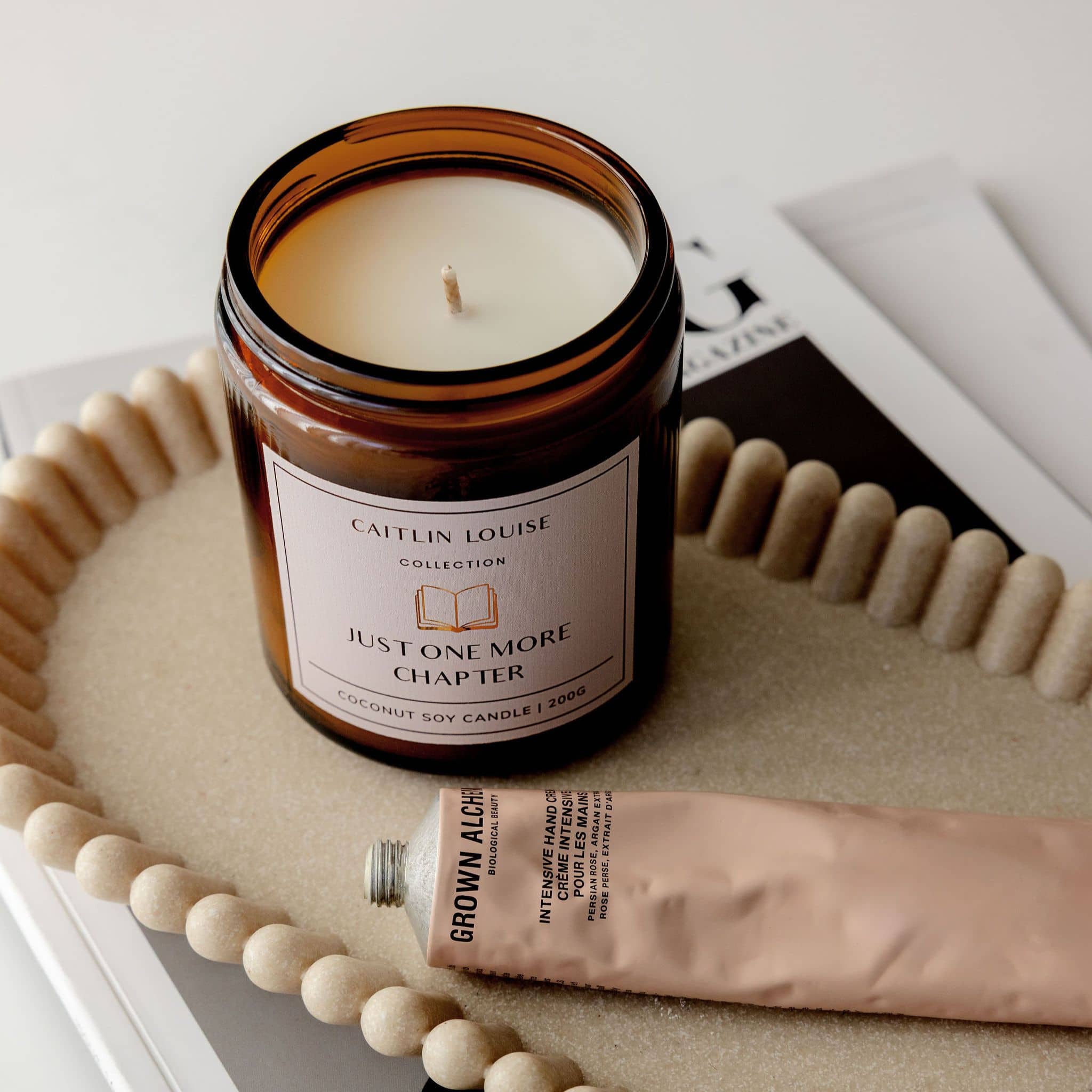 Candle in a glass jar with a label saying "Just One More Chapter" on a textured surface