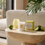 Candle and packaging on a wooden table with limes and a leaf in a living room setting