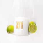 Stylised imagery of clear plastic bag containing Caitlin Louise Collection candle and green limes on a white background