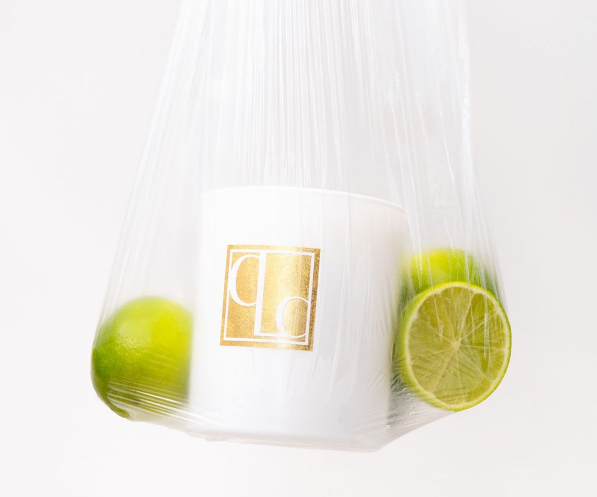 Stylised imagery of clear plastic bag containing Caitlin Louise Collection candle and green limes on a white background