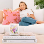 Caitlin Louise Collection's Patchouli and Sandalwood candle sitting on stack of books with woman on the lounge in the background.