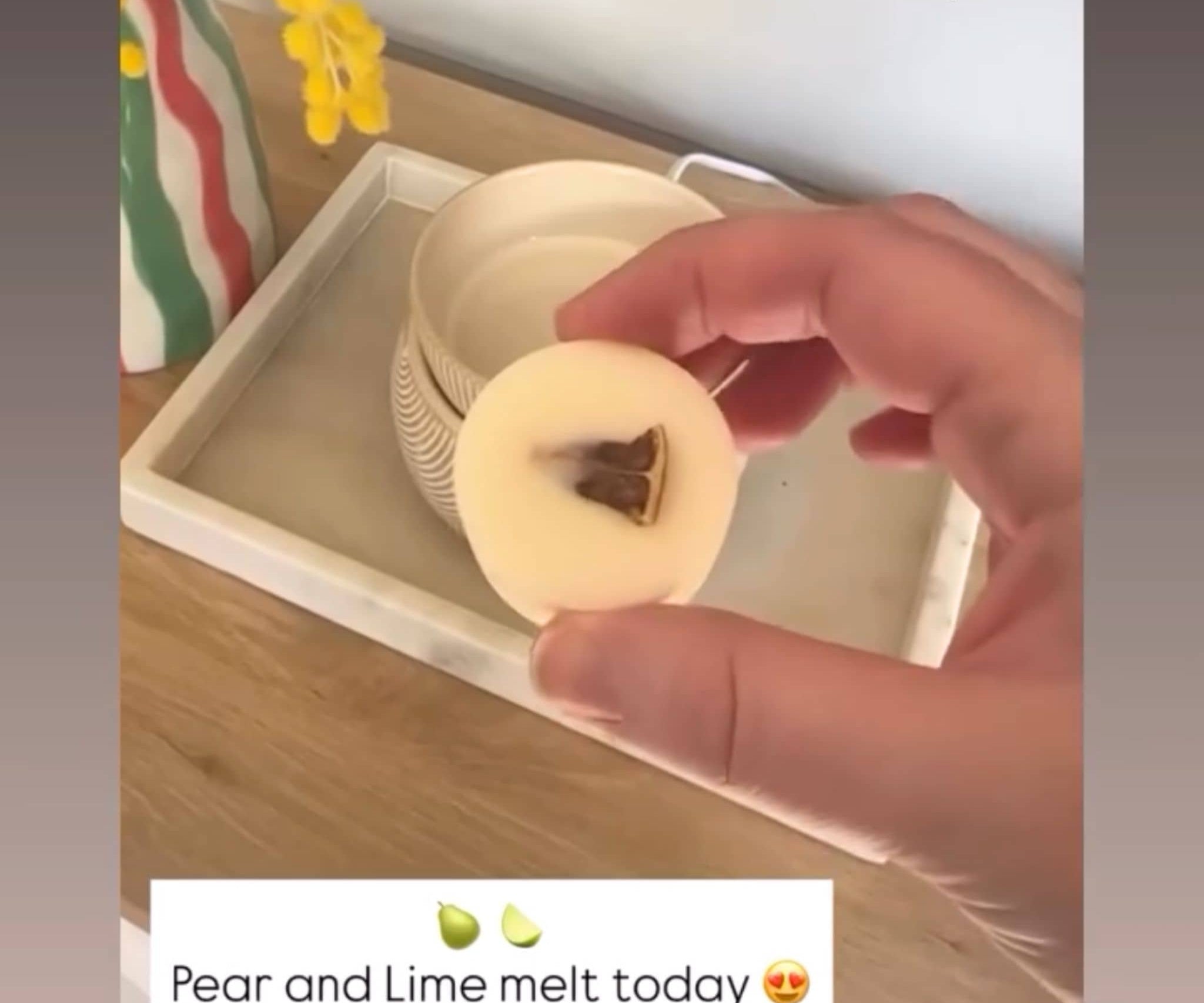 Hand holding a wax melt disk with a dried lime center on a wooden surface, with text indicating a customer post on Instagram.