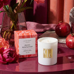 Candle with packaging and flowers on a reflective surface