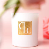 Caitlin Louise Collection white candle with gold logo on a pink background