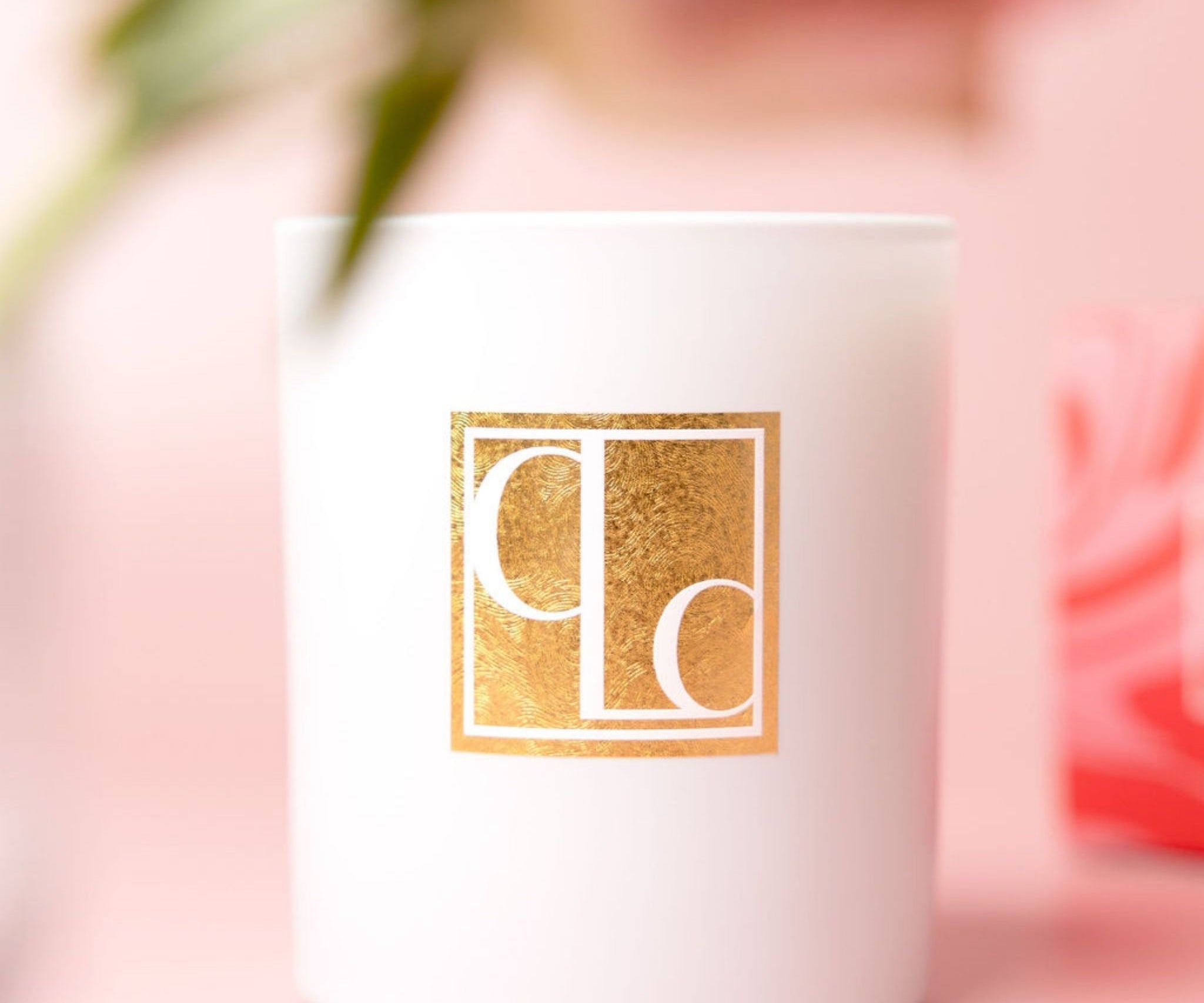 Caitlin Louise Collection white candle with gold logo on a pink background