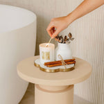 Hand lighting a candle on a small round table with decorative elements.