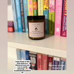 Candle labeled 'Give Me That Slow Burn Romance' on a shelf with books in the background