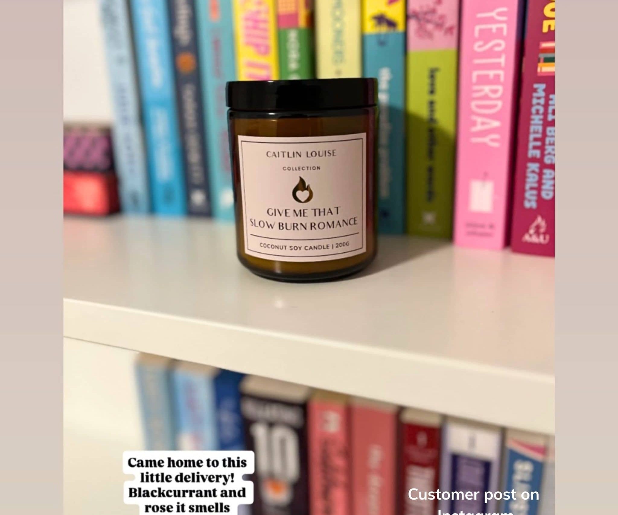 Candle labeled 'Give Me That Slow Burn Romance' on a shelf with books in the background