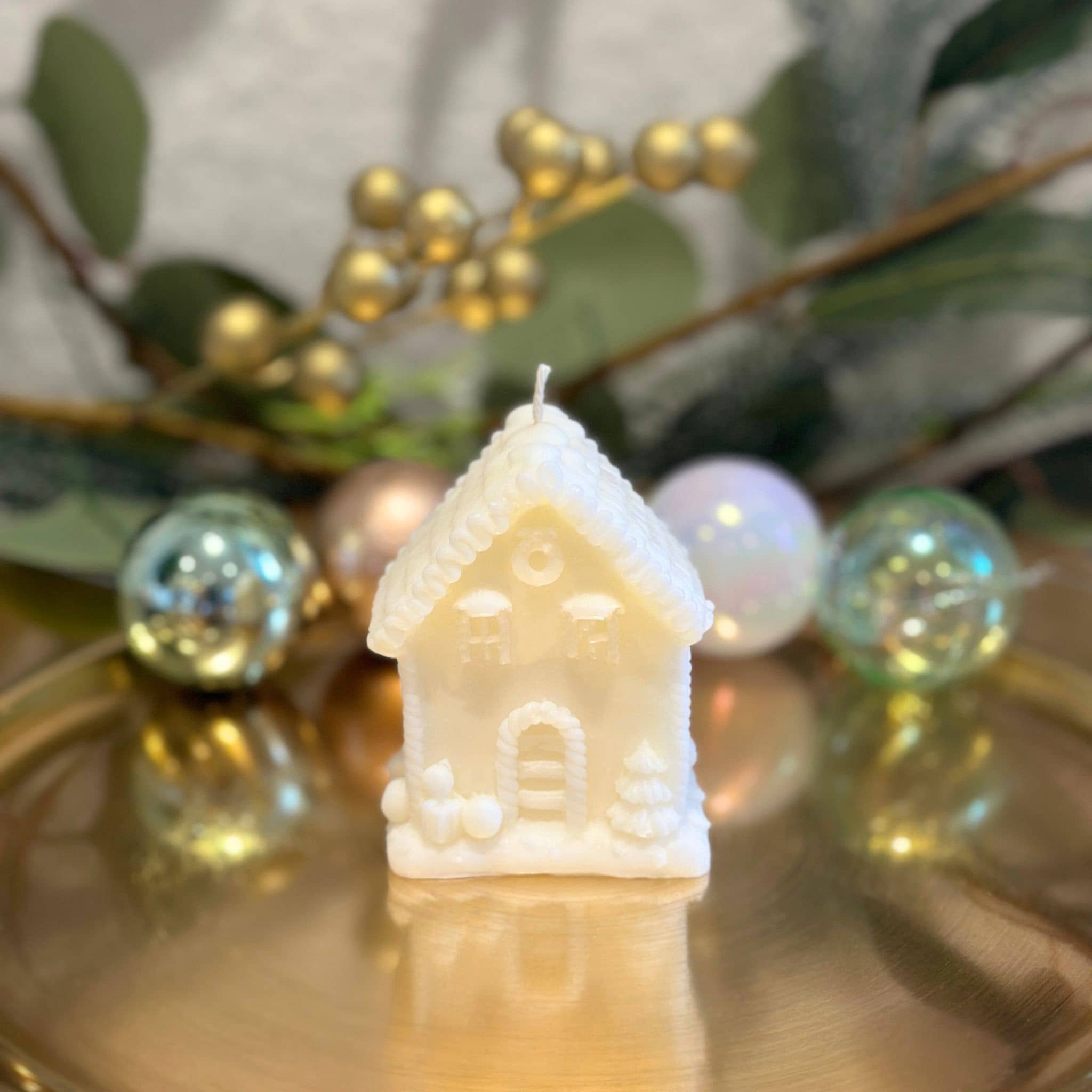 Caitlin Louise Collection's tiny christmas house sculptural candle - on gold plate with wreath in background