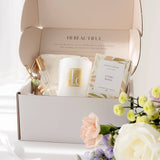 Gift box with a candle, room spray, and keyring, surrounded by flowers on a light background.