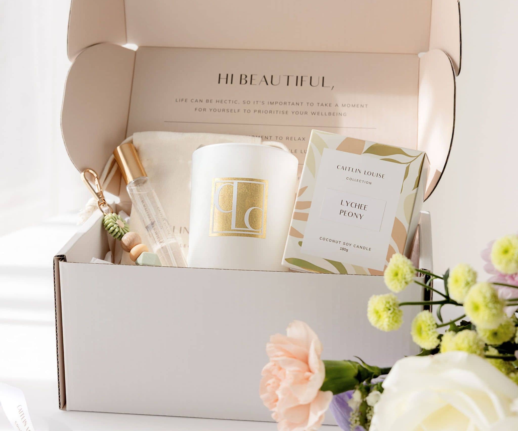 Gift box with a candle, room spray, and keyring, surrounded by flowers on a light background.