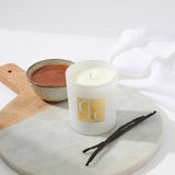 Caitlin Louise Collection Vanilla Caramel Scented Candle on board with bowl of caramel in background and vanilla sticks in the foreground.