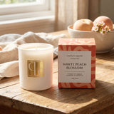 Candle and packaging of 'White Peach Blossom' candle from Caitlin Louise Collection on a wooden surface.