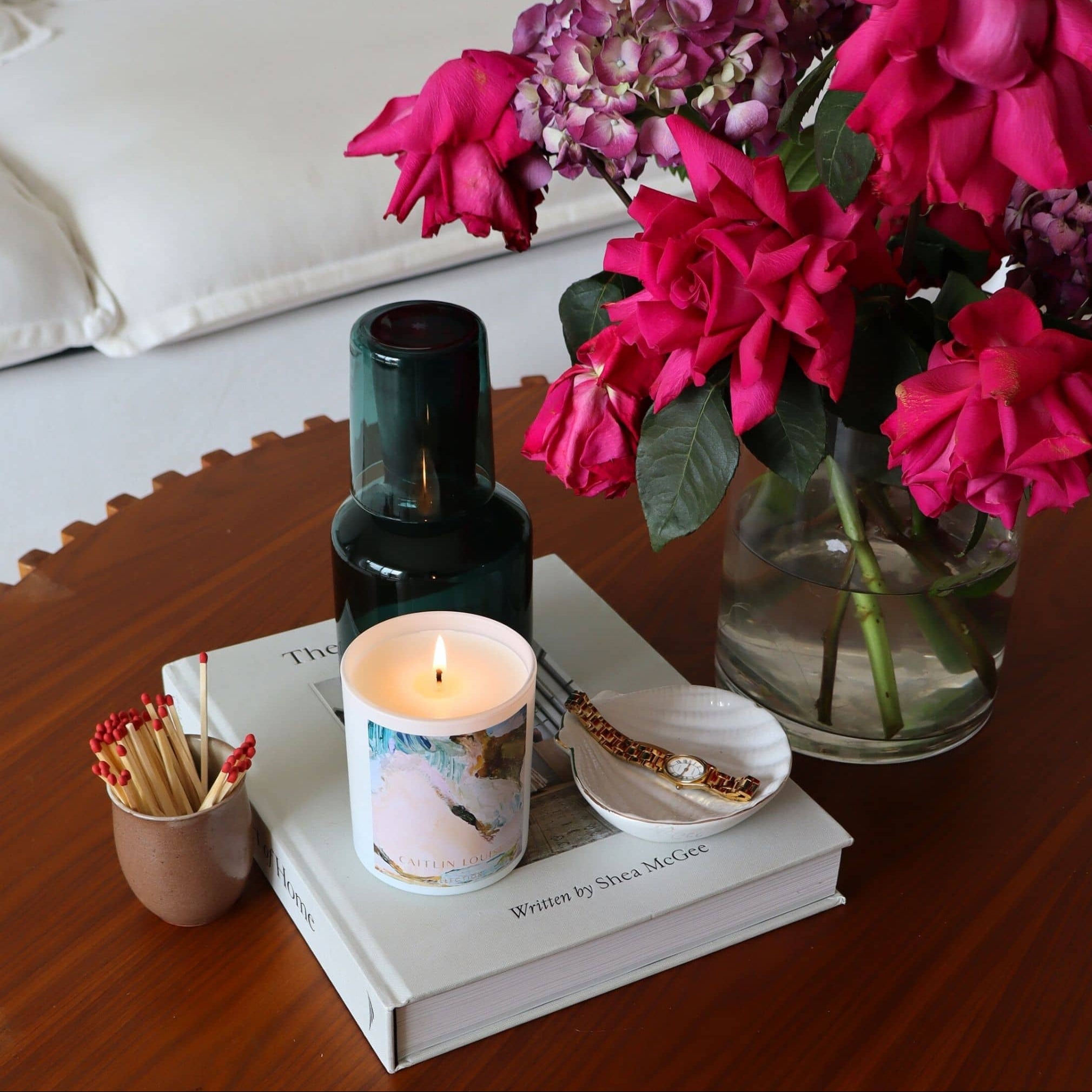 Wood Sage and Sea Salt Candle, matches, book, and vase with flowers on a wooden surface
